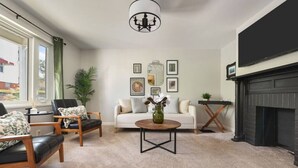Una sala de estar con sofá, dos sillones, una mesa de centro, chimenea y cuadros en la pared.