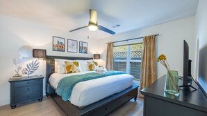 A modern bedroom with a bed, bedside tables, a ceiling fan, and a window with curtains.