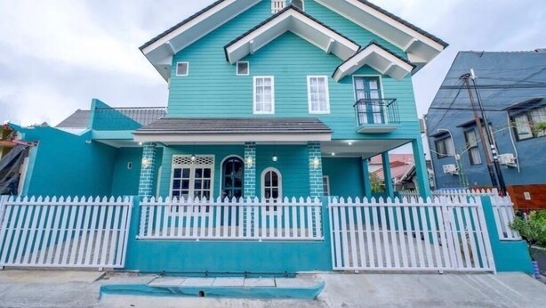 Una casa de dos pisos con cerca blanca de piquetes, un balcón y un pequeño porche.