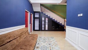 Un pasillo con un sofá marrón, un tapete estampado, una escalera y una puerta roja.