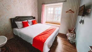 Un dormitorio con cama, ventana, mesita de noche y perchero.