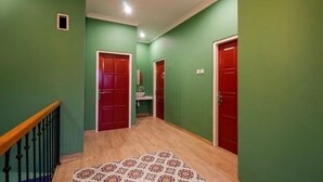 Un pasillo con paredes verdes, suelo de madera y puertas rojas.