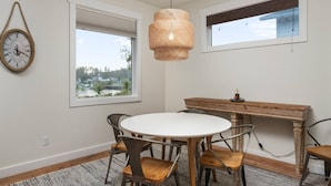 Un comedor con una mesa redonda, cuatro sillas, un banco de madera y dos ventanas con vistas al paisaje.
