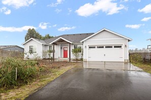 Une maison de plain-pied avec un garage, une porte rouge et une allée.