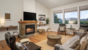 Una sala de estar con chimenea, televisor, sofá y vistas al exterior.