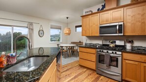 Una cocina moderna con armarios de madera, electrodomésticos de acero inoxidable, encimera de granito y vistas al exterior.