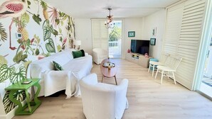 A living room with a white sofa, a white armchair, a small round table, and a TV.