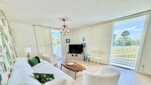 A spacious living room with a sofa set, a coffee table, a TV, and a balcony with a view.