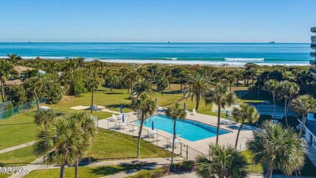A resort with a swimming pool, palm trees, and a view of the ocean.