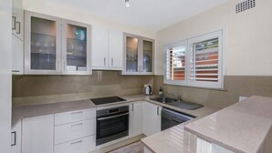 A modern kitchen with white cabinets, a built-in oven, a sink, and a window with blinds.