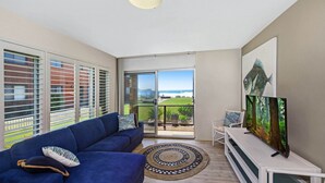 A modern living room with a blue sofa, a round rug, and a TV on a white stand.