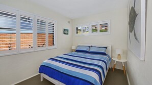 A bedroom with a bed, two bedside tables, and two windows with blinds.