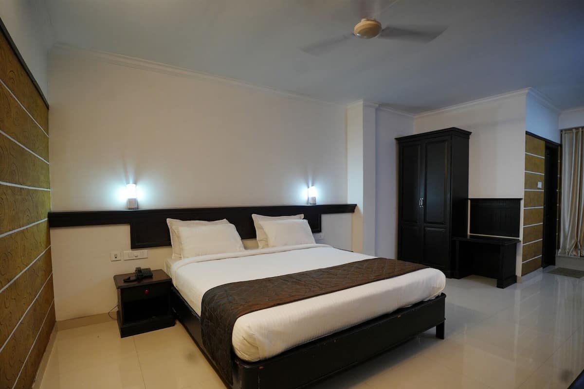 A hotel room with a large bed, two bedside lamps, a ceiling fan, a wardrobe, and a TV.