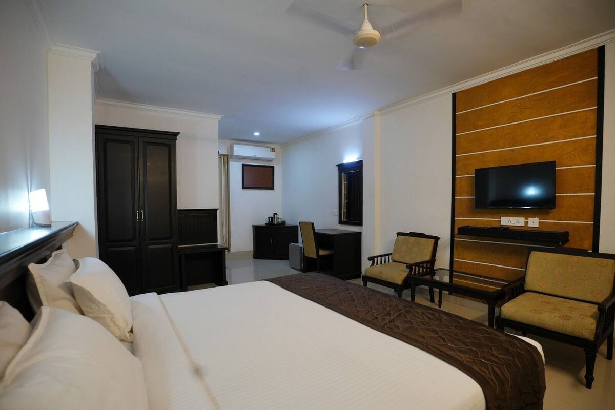 A hotel room with a large bed, a desk, a chair, a television mounted on the wall, and a wardrobe.