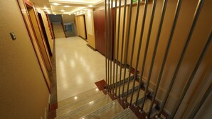 Pasillo de hotel con una escalera que conduce a un piso superior, con un letrero de salida de incendios y una puerta de seguridad.