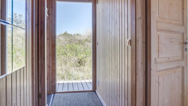 A wooden hallway with a door leading outside, a window on the left, and a door on the right.