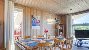 A dining area with a wooden table, chairs, a hanging light, a bookshelf, and a TV.