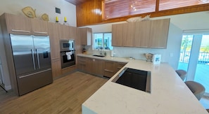 A modern kitchen with stainless steel appliances, wooden cabinets, and a large island with a black sink.