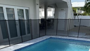 Et rektangulært swimmingpool med klart, blåt vand, omgivet af en hvid flisegang og et sort hegn.