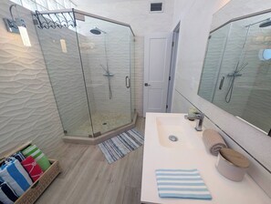 A modern bathroom with a glass-enclosed shower, a large mirror, and a wooden floor.