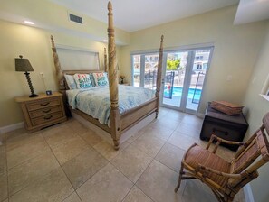 A four-poster bed with a canopy, a nightstand with a lamp, a wicker chair, and a suitcase. - Beautiful Canal front Home with Above Ground Pool, Dock and Fish Cleaning Station (Key Largo)