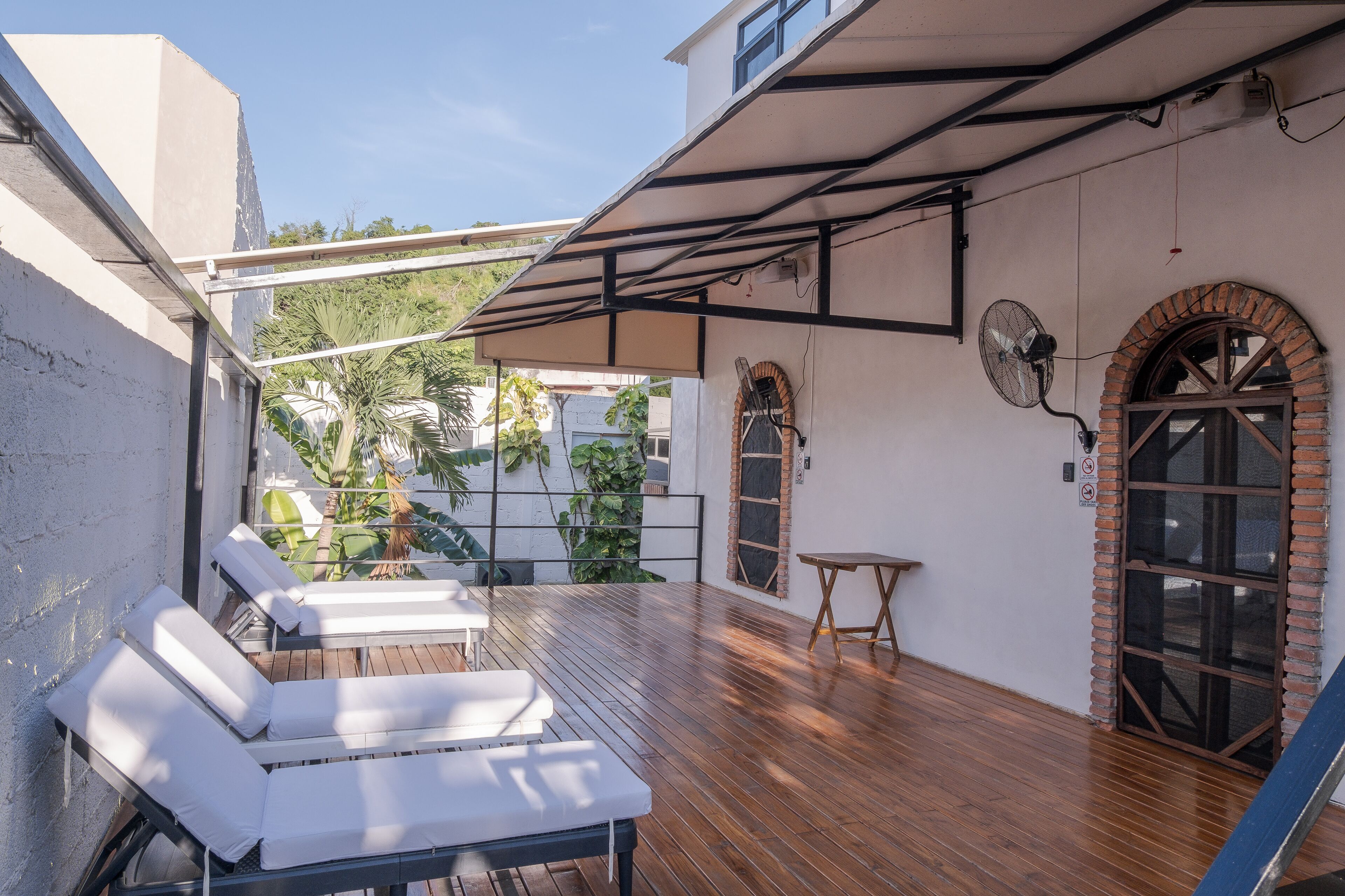 Una terraza en la azotea con suelo de madera, sillas de lounge blancas, una mesita y un arco de ladrillo.