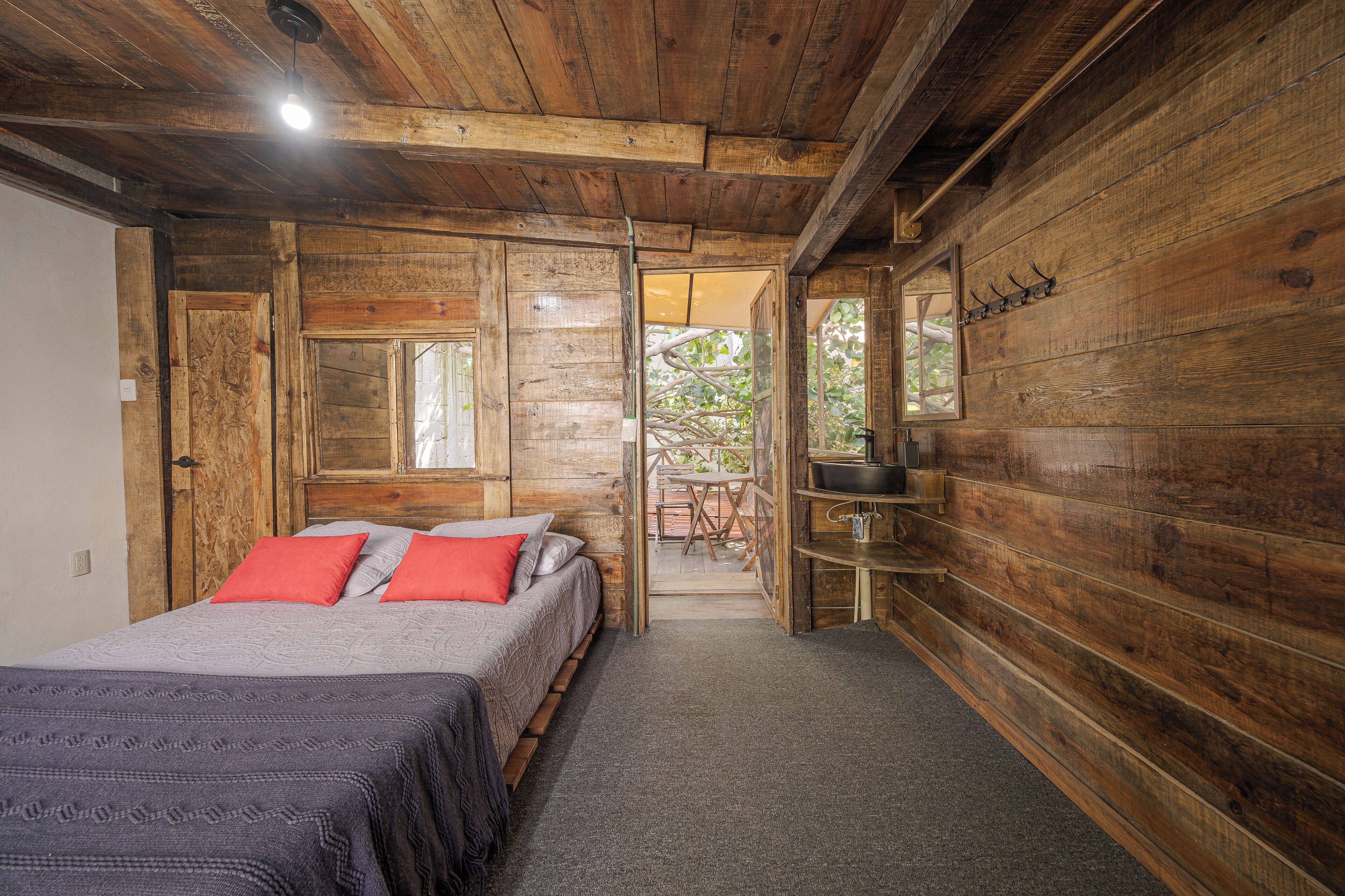 Ein Schlafzimmer einer Holzhütte mit einem Bett, einem kleinen Tisch und Blick ins Freie.