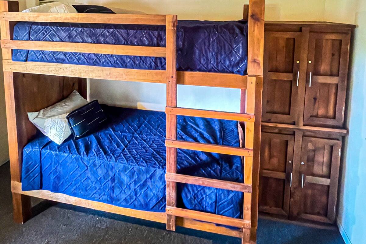 A bunk bed with a blue mattress, wooden frame, and a headboard.