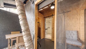 A wooden interior with a table and chairs, a glass shower, and a grey upholstered chair. - El Refugio de Sayulita - Solo Adultos (Sayulita)
