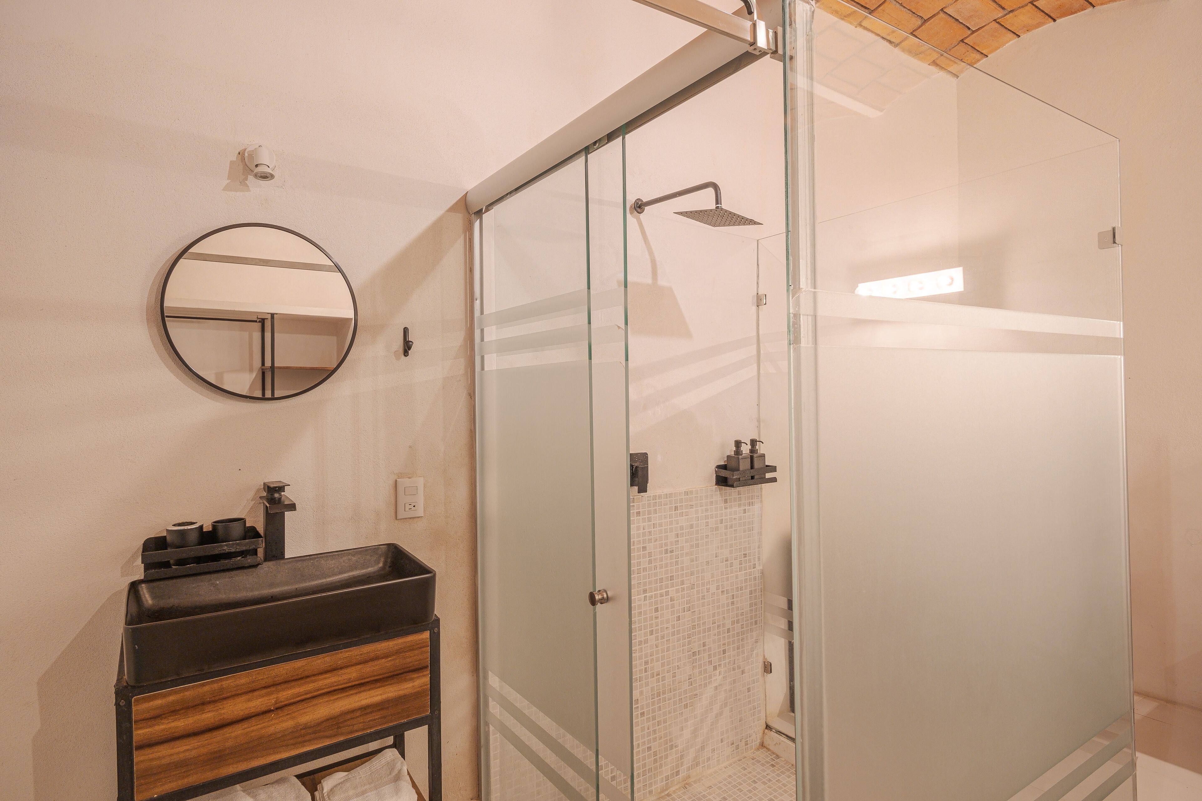 A modern bathroom with a glass-enclosed shower, a round mirror, and a wooden vanity.