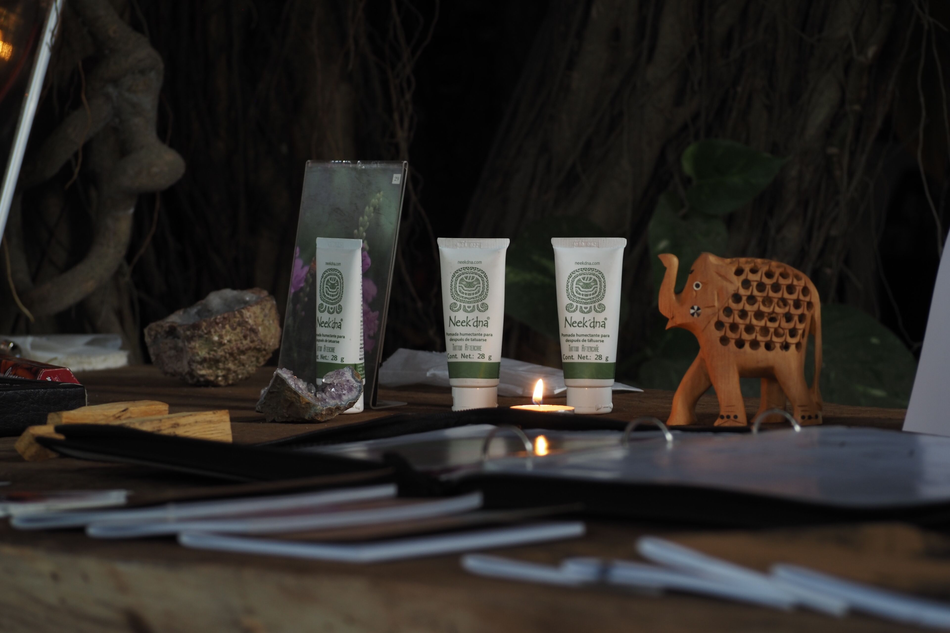 A wooden table with a laptop, a candle, and three tubes of Neekdhna cream.