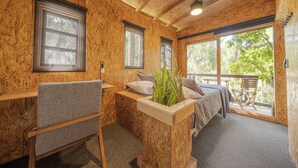 A cozy room with a bed, a chair, a small table, and a window overlooking greenery. - El Refugio de Sayulita - Solo Adultos (Sayulita)