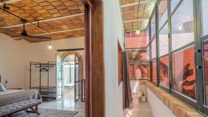 A bedroom with a bed, a bench, a ceiling fan, and a view through large windows. - El Refugio de Sayulita - Solo Adultos (Sayulita)