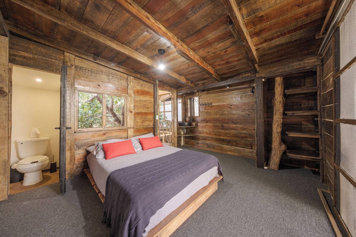 A wooden cabin bedroom with a bed, a toilet, and a window.
