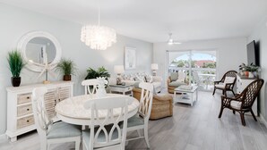 A modern living room with a dining area, a round table, and a large window with a view. - Breakers West C2 | Stunning Top Floor Beach Residence | Steps to the Sand (Sanibel)