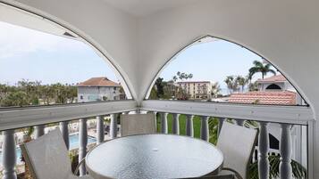Varanda com mesa redonda e cadeiras, com vista para uma piscina e edifícios.
