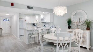 A modern kitchen with white cabinetry, a dining area with white chairs, and a round table. - Breakers West C2 | Stunning Top Floor Beach Residence | Steps to the Sand (Sanibel)