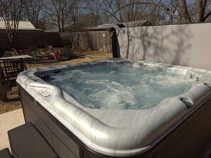 Un jacuzzi con panel de control, rodeado por una terraza de madera y mobiliario exterior.