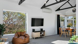 Ein modernes Wohnzimmer mit großem Fenster, einem Flachbildfernseher, einem Sitzsack, einem Esstisch mit Stühlen und einer kleinen Pflanze.