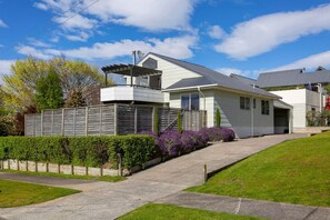 A modern two-story house with a covered porch, a garage, and a well-maintained garden with purple flowers.