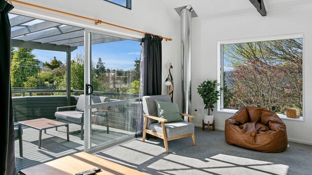 Ein modernes Wohnzimmer mit Glastür zu einem Außenbalkon, einem braunen Ledersessel und einem Blumentopf.