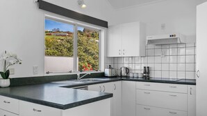 Eine moderne Küche mit weißen Schränken, einer schwarzen Arbeitsplatte, einem Fenster mit Blick auf Grünflächen und einer eingebauten Dunstabzugshaube.
