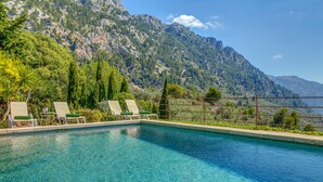 Ein Pool mit Liegestühlen, umgeben von viel Grün und Bergen.
