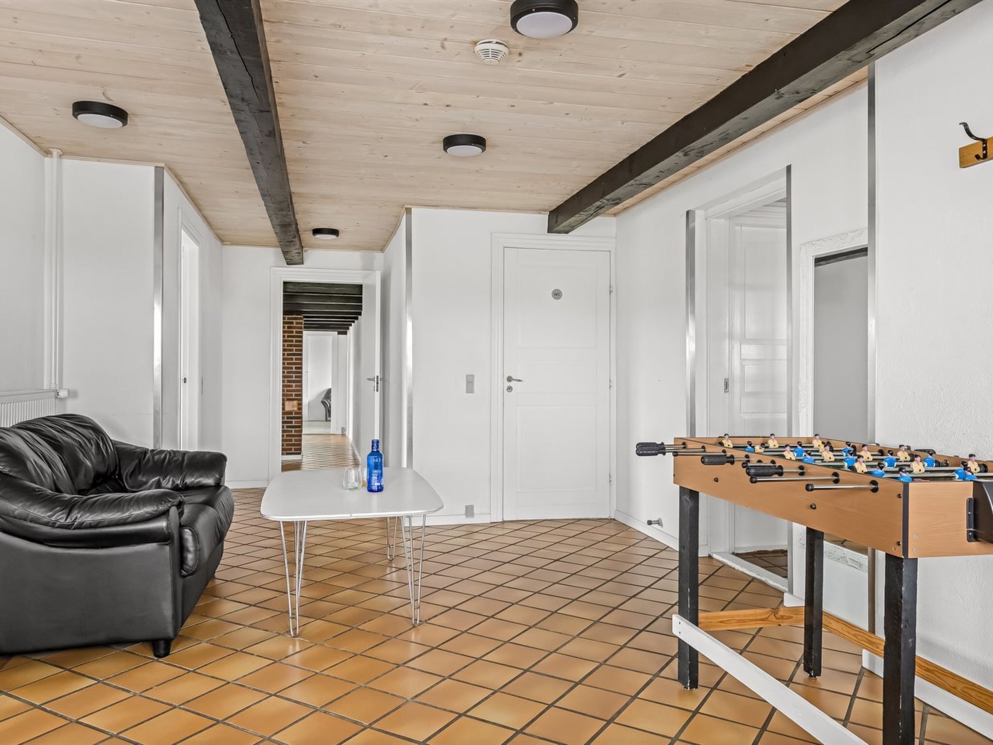 Una habitación con una mesa de fútbol de mesa, un sofá de cuero negro y piso de baldosas.