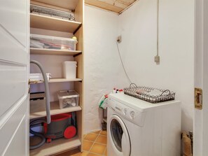 Ett tvättrum med tvättmaskin, hyllor med förvaringslådor och en dammsugare.