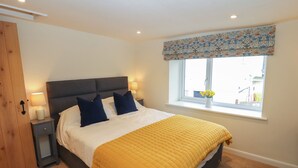 A bedroom with a bed, two bedside lamps, a window with a view, and a wooden door. - Cobble Cottage (Keswick)