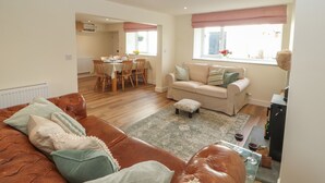 A living room with a brown leather sofa, a beige sofa, and a glass coffee table. There is a dining area with a table and chairs in the background. - Cobble Cottage (Keswick)
