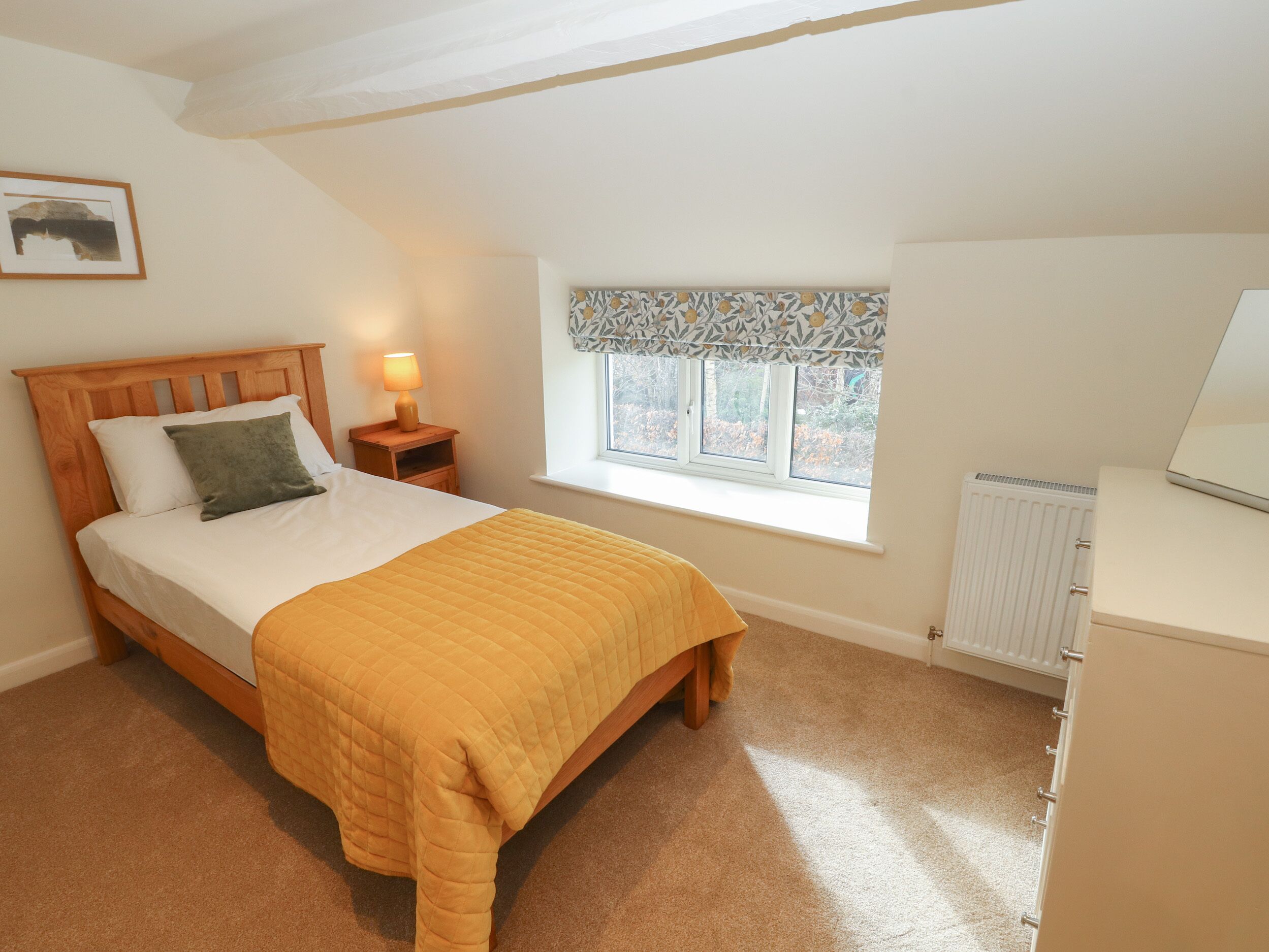 A bedroom with a bed, a nightstand, a window, and a radiator.