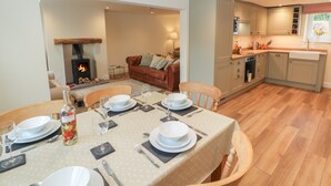 A dining area with a table set for four, a fireplace, a kitchen with modern appliances, and a cozy living space with a sofa. - Cobble Cottage (Keswick)