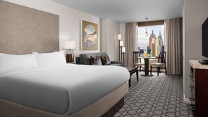 A hotel room with a large bed, a desk, a chair, and a view of the cityscape.